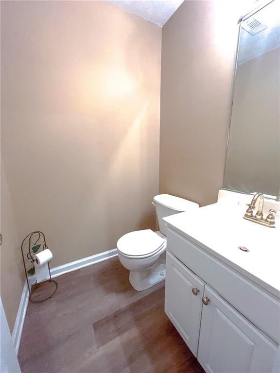 half bathroom with vanity, baseboards, wood finished floors, and toilet