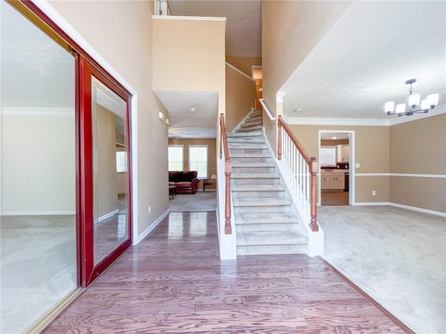 carpeted foyer featuring crown molding, baseboards, a notable chandelier, and stairway
