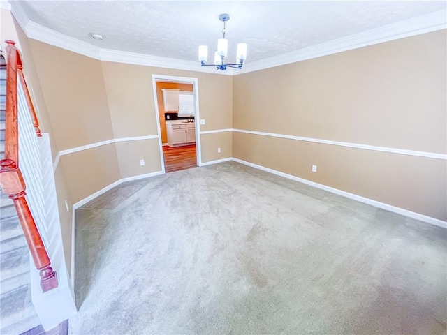unfurnished room with carpet floors, ornamental molding, baseboards, and a chandelier