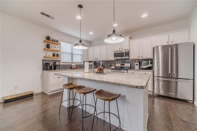 kitchen featuring pendant lighting, white cabinetry, stainless steel appliances, light stone counters, and a center island with sink