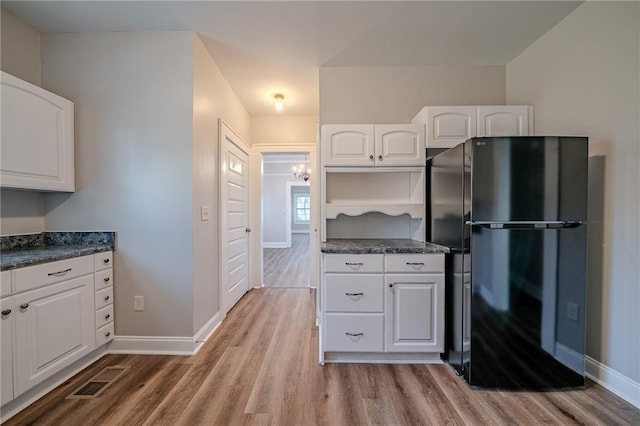 kitchen with black refrigerator, white cabinetry, and light wood-type flooring