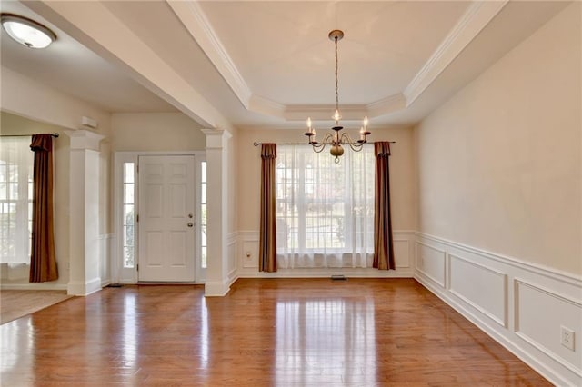 foyer featuring a tray ceiling, hardwood / wood-style flooring, decorative columns, and an inviting chandelier