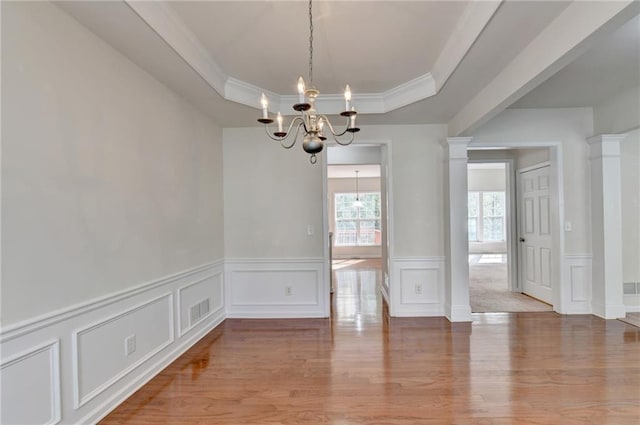 unfurnished dining area with ornate columns, hardwood / wood-style flooring, a tray ceiling, crown molding, and a chandelier