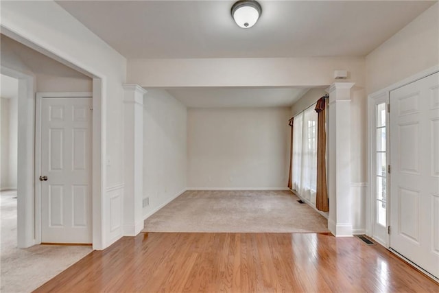 foyer entrance with light hardwood / wood-style floors, decorative columns, and a wealth of natural light