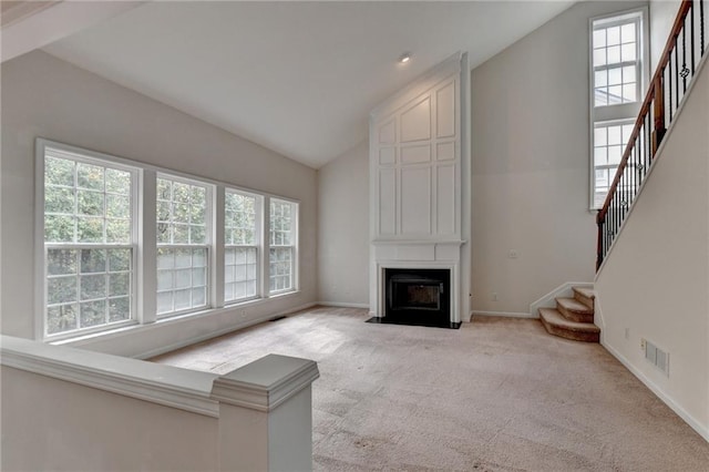 unfurnished living room with vaulted ceiling, light colored carpet, and a healthy amount of sunlight