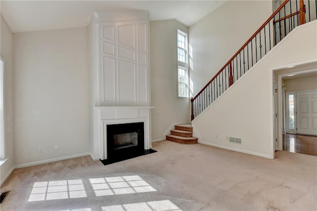 unfurnished living room with a large fireplace, high vaulted ceiling, and light colored carpet