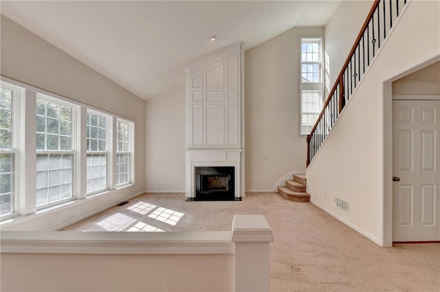 unfurnished living room featuring a large fireplace, light carpet, lofted ceiling, and plenty of natural light