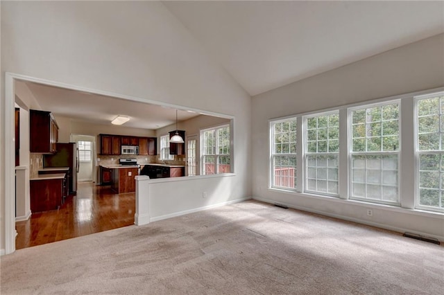 unfurnished living room with high vaulted ceiling and dark colored carpet