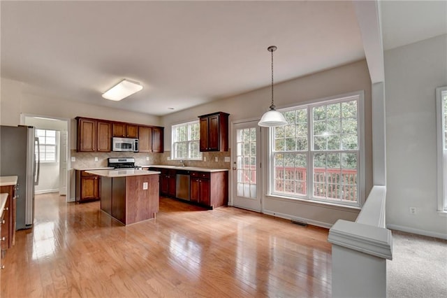 kitchen featuring backsplash, a center island, stainless steel appliances, pendant lighting, and light hardwood / wood-style flooring