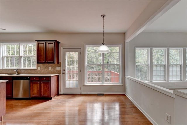 kitchen featuring decorative backsplash, dishwasher, light wood-type flooring, and decorative light fixtures