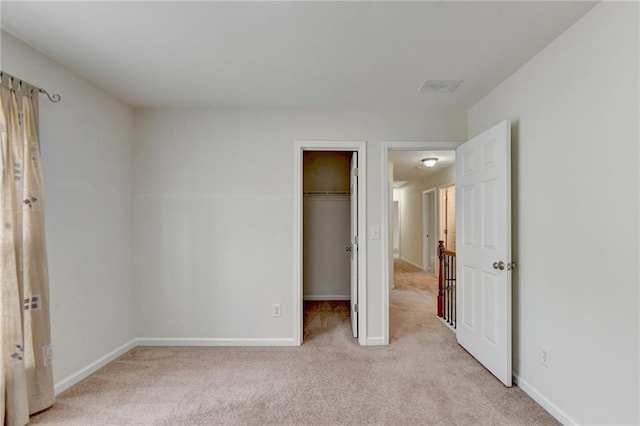 unfurnished bedroom with a spacious closet, a closet, and light colored carpet