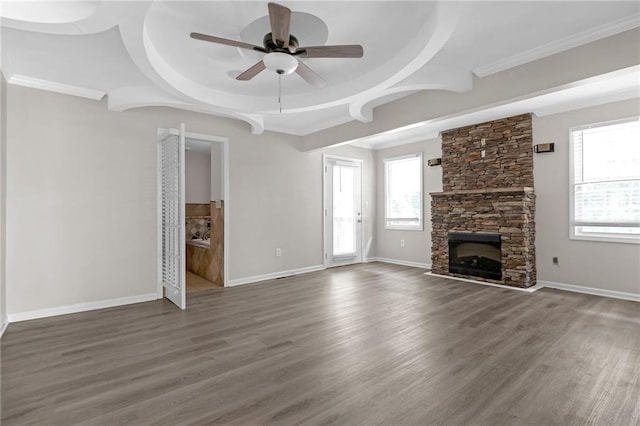 unfurnished living room featuring ceiling fan, a healthy amount of sunlight, dark hardwood / wood-style flooring, and a stone fireplace