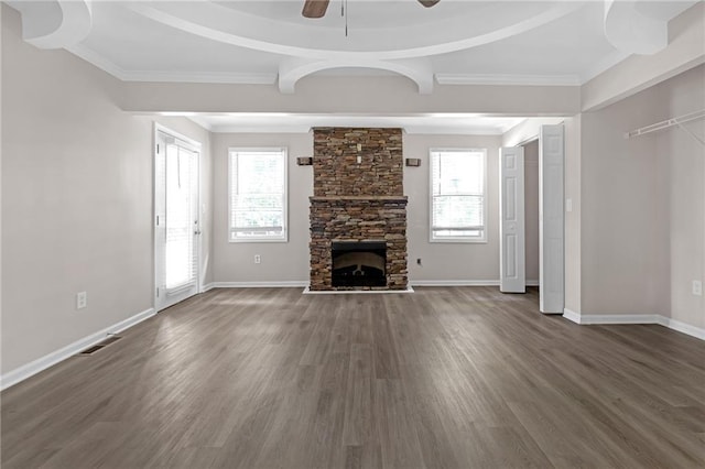 unfurnished living room with ceiling fan, dark hardwood / wood-style flooring, ornamental molding, and a stone fireplace