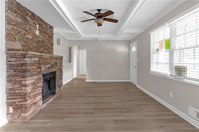 unfurnished living room featuring ceiling fan, wood-type flooring, a stone fireplace, and beamed ceiling