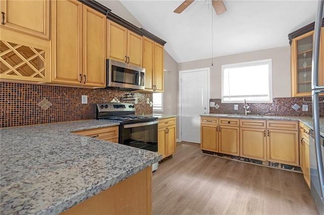 kitchen with light stone countertops, appliances with stainless steel finishes, light hardwood / wood-style floors, sink, and vaulted ceiling