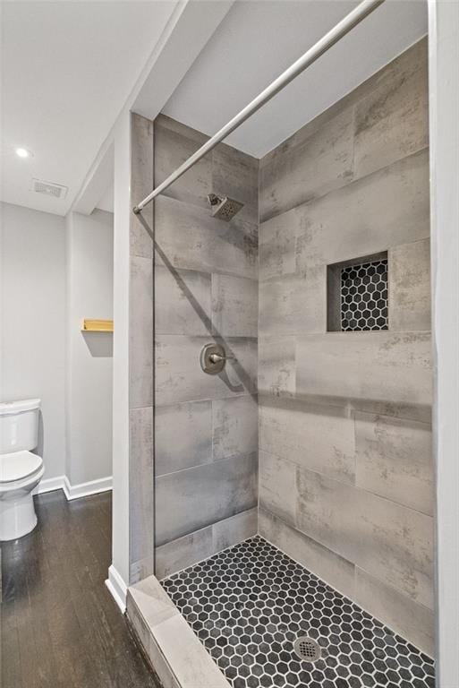 bathroom with hardwood / wood-style flooring, tiled shower, and toilet