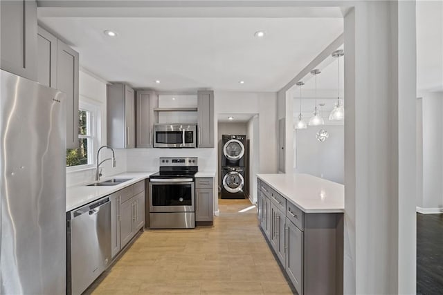 kitchen featuring gray cabinets, stacked washing maching and dryer, sink, hanging light fixtures, and stainless steel appliances