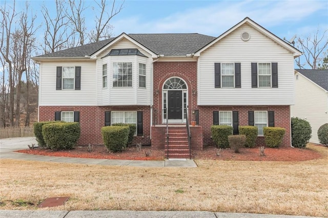 split foyer home featuring brick siding, roof with shingles, and a front yard