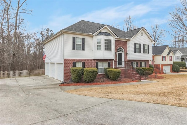 raised ranch with a garage, concrete driveway, brick siding, and fence