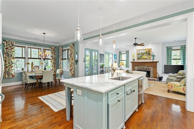 kitchen with light stone countertops, dark hardwood / wood-style floors, hanging light fixtures, a kitchen island with sink, and ceiling fan