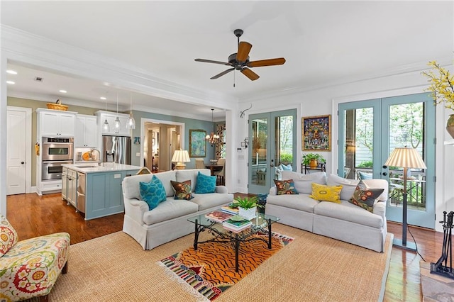 living room with ceiling fan with notable chandelier, ornamental molding, french doors, and light hardwood / wood-style floors