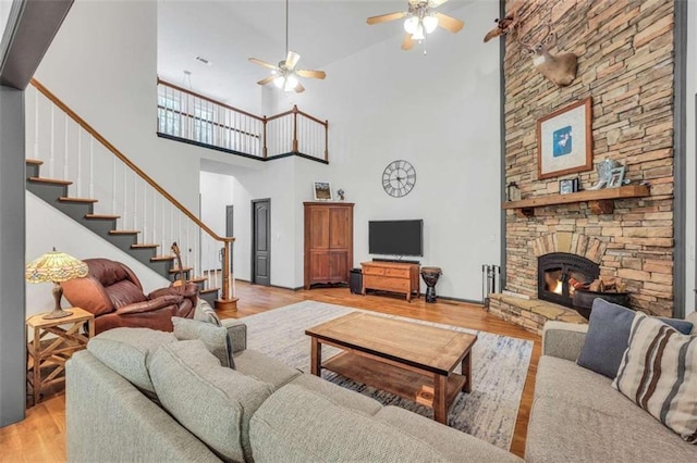 living room with light wood finished floors, stairs, a fireplace, ceiling fan, and a towering ceiling