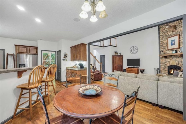 dining area with a textured ceiling, light wood finished floors, stairs, a stone fireplace, and a notable chandelier