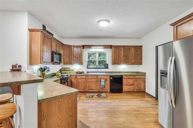 kitchen with a sink, a peninsula, brown cabinets, light wood-type flooring, and black appliances