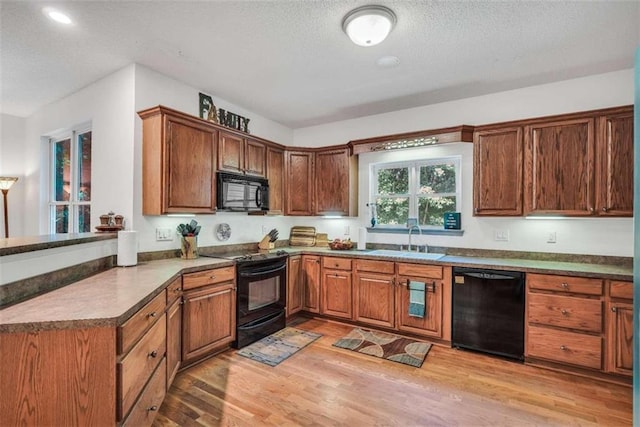 kitchen featuring a sink, a textured ceiling, light wood-type flooring, brown cabinetry, and black appliances
