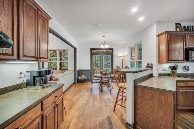 kitchen with light wood-style flooring, dark countertops, black microwave, an inviting chandelier, and a kitchen breakfast bar
