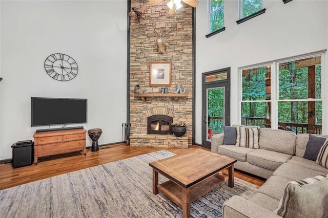 living area featuring a towering ceiling, a healthy amount of sunlight, a fireplace, and wood finished floors