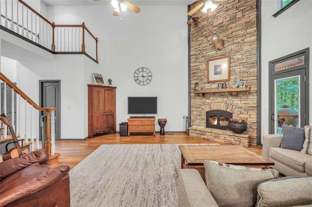 living room featuring stairs, a ceiling fan, a fireplace, a high ceiling, and wood finished floors