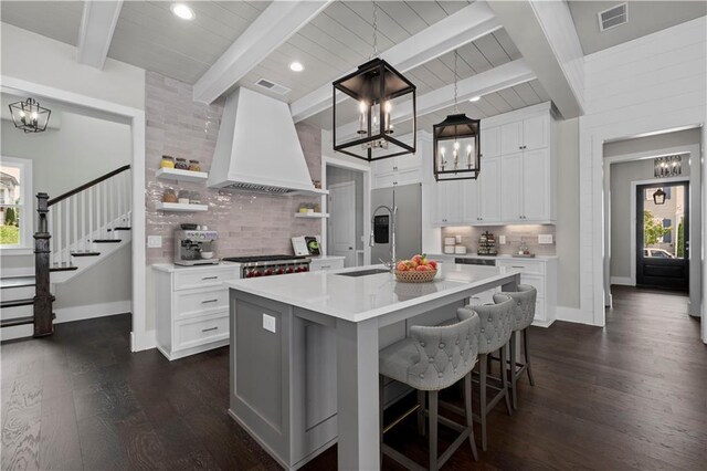 kitchen with decorative backsplash, sink, beam ceiling, dark hardwood / wood-style floors, and a center island with sink