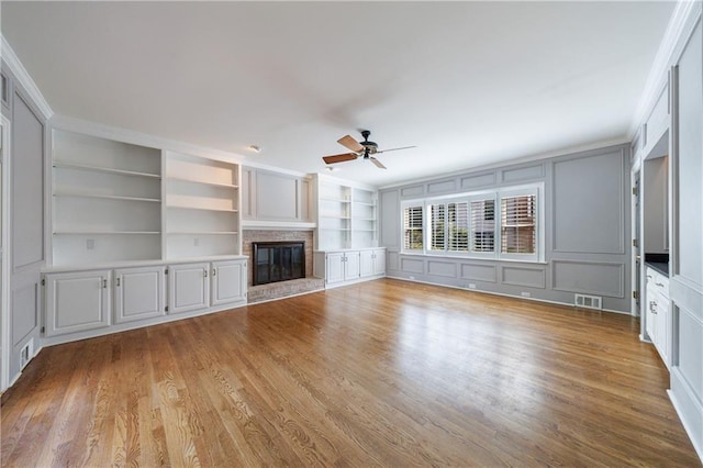 5004 Haralson Way SW, Lilburn, GA 30047 - unfurnished living room with a ceiling fan, light wood-style flooring, a glass covered fireplace, built in shelves, and a decorative wall