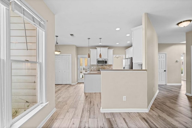 kitchen featuring fridge with ice dispenser, visible vents, stainless steel microwave, white cabinets, and decorative backsplash