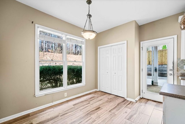 unfurnished dining area with a wealth of natural light, light wood finished floors, and baseboards