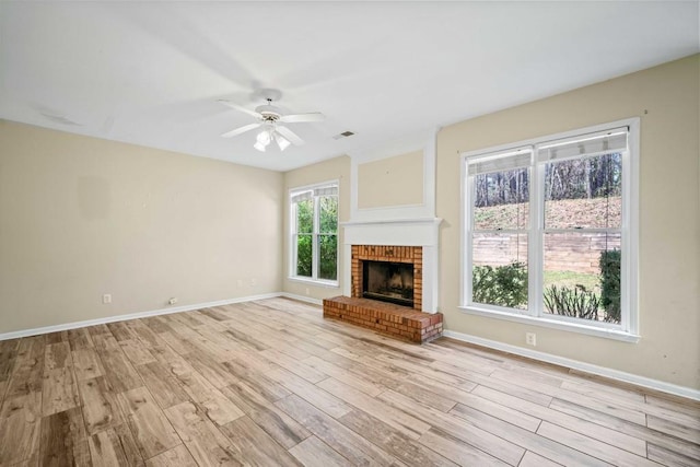 unfurnished living room featuring light wood finished floors, visible vents, a brick fireplace, baseboards, and a ceiling fan