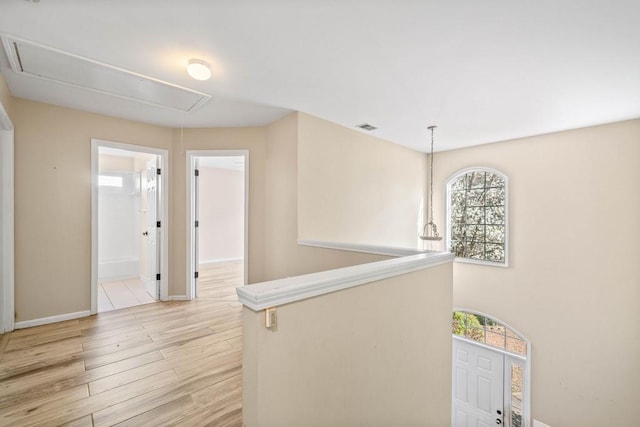 corridor featuring light wood finished floors, visible vents, attic access, and baseboards