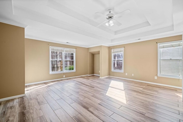 empty room featuring light wood-style flooring, baseboards, crown molding, a raised ceiling, and ceiling fan