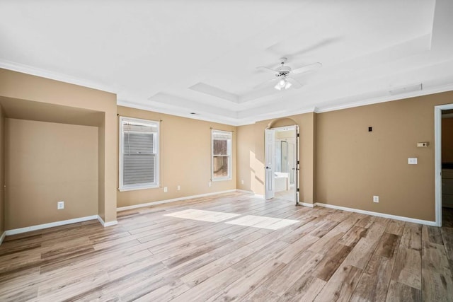 empty room featuring baseboards, a tray ceiling, ornamental molding, light wood-style floors, and a ceiling fan