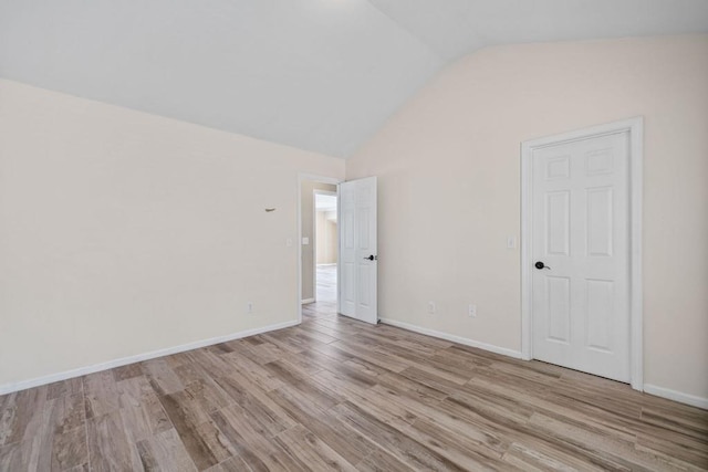 spare room featuring vaulted ceiling, baseboards, and light wood finished floors