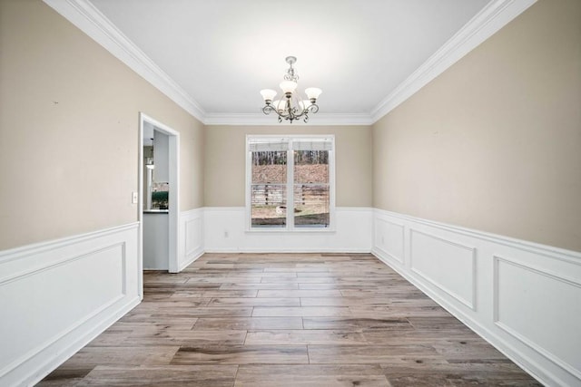 unfurnished dining area featuring a notable chandelier, wood finished floors, a wainscoted wall, and ornamental molding