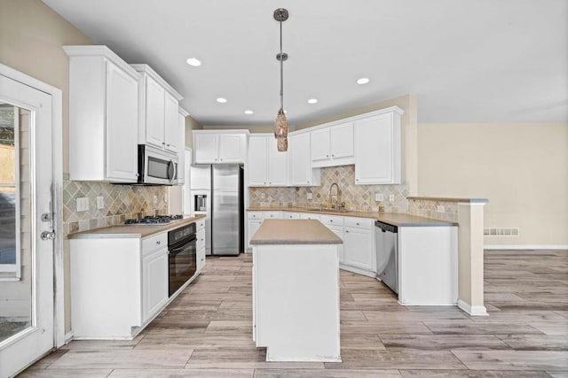 kitchen with visible vents, a sink, a kitchen island, white cabinetry, and appliances with stainless steel finishes