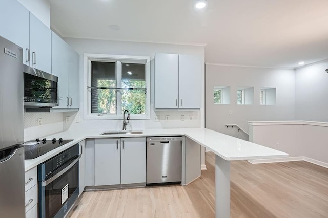 kitchen with stainless steel appliances, light hardwood / wood-style flooring, decorative light fixtures, white cabinets, and ornamental molding