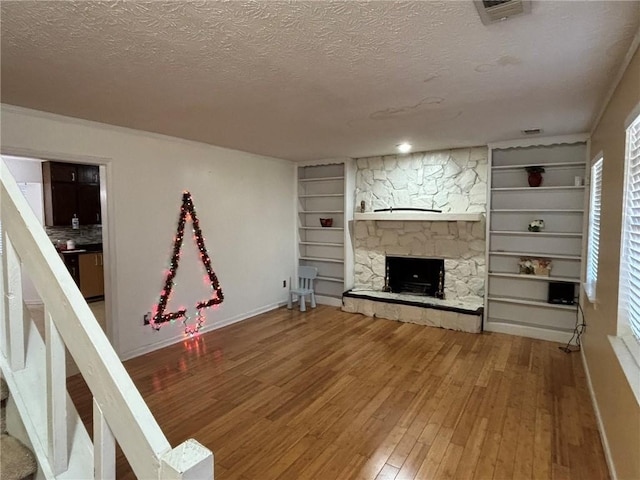 unfurnished living room featuring built in shelves, hardwood / wood-style floors, a textured ceiling, and a stone fireplace