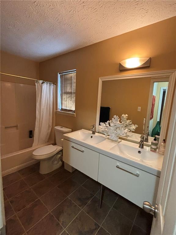 full bathroom featuring vanity, toilet, a textured ceiling, and shower / bathtub combination with curtain