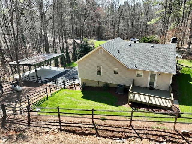 back of property with cooling unit, a forest view, a wooden deck, a yard, and a shingled roof