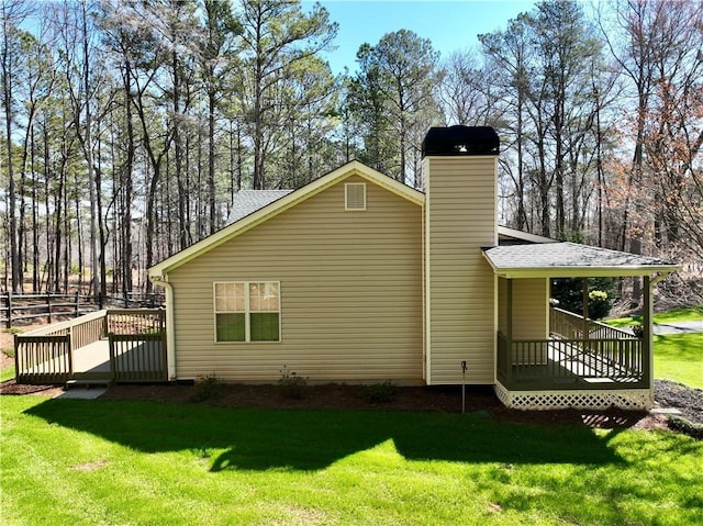 view of side of home with a wooden deck, a lawn, a chimney, and a shingled roof