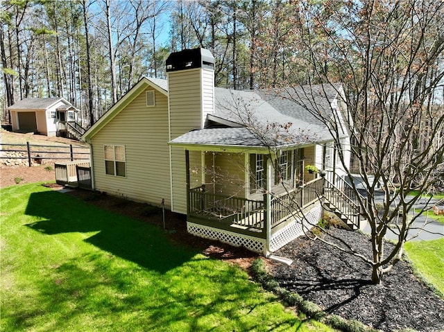 view of side of home with a chimney, roof with shingles, a yard, and fence