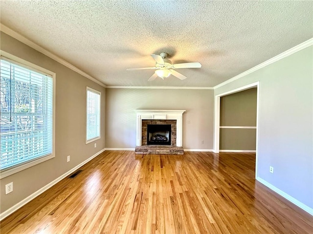 unfurnished living room featuring light wood-type flooring, ceiling fan, a fireplace, and crown molding